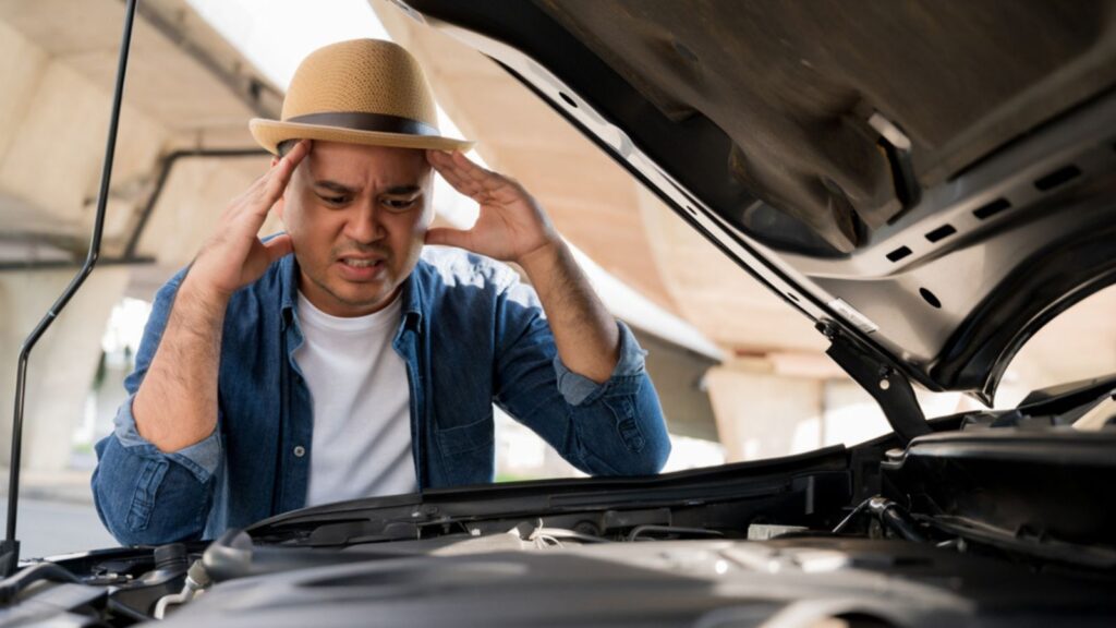 A man stood stressed in front of a car hood