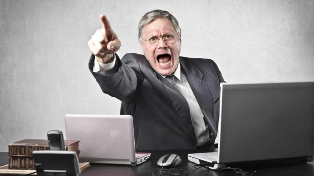 Angry senior businessman sitting at his desk and screaming