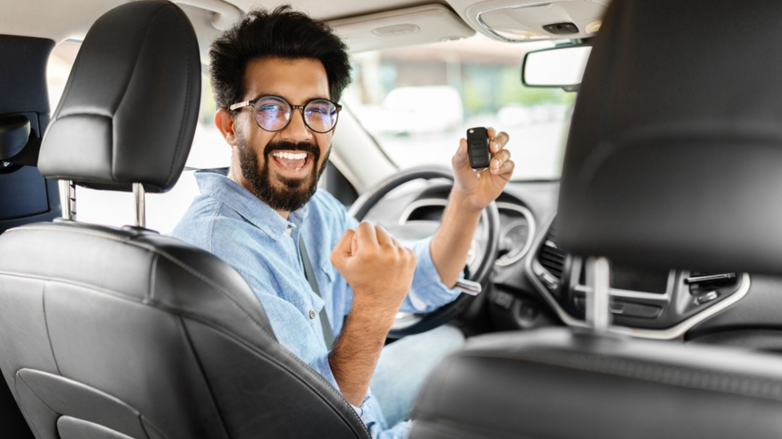 Cheerful arab man holding key from auto, buying brand new car in showroom