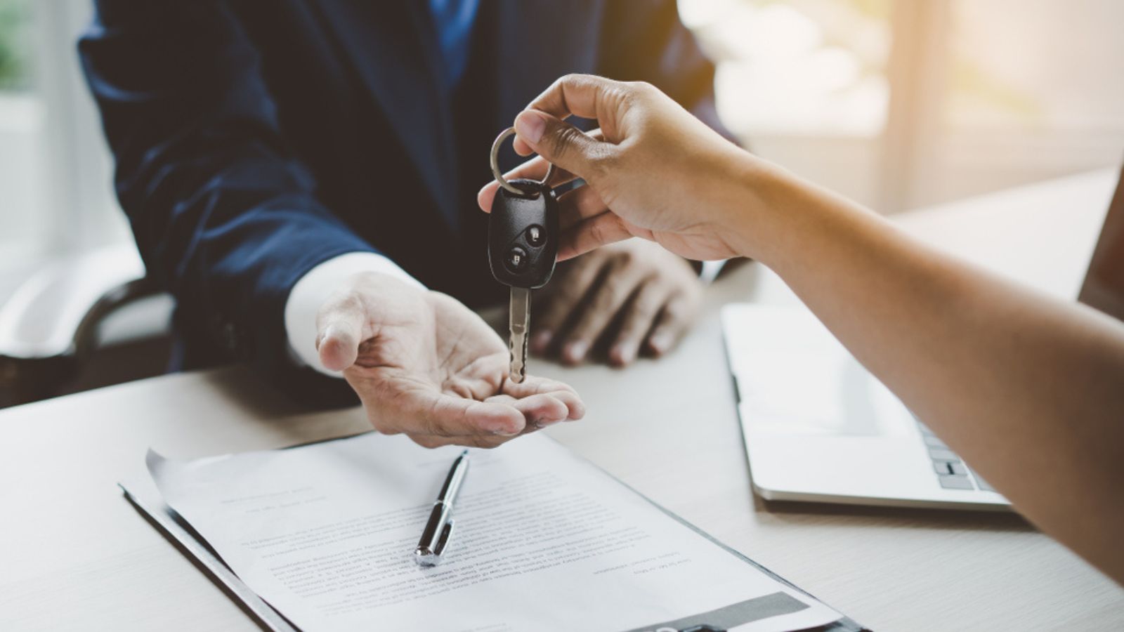 Close up view Hand of agent giving car key to customer after signed rental contract form