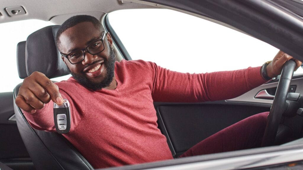 Happy handsome african man showing car keys in his newly bought auto smiling cheerfully sitting in the luxury vehicle copyspace owner ownership sales driving consumerism private taxi concept