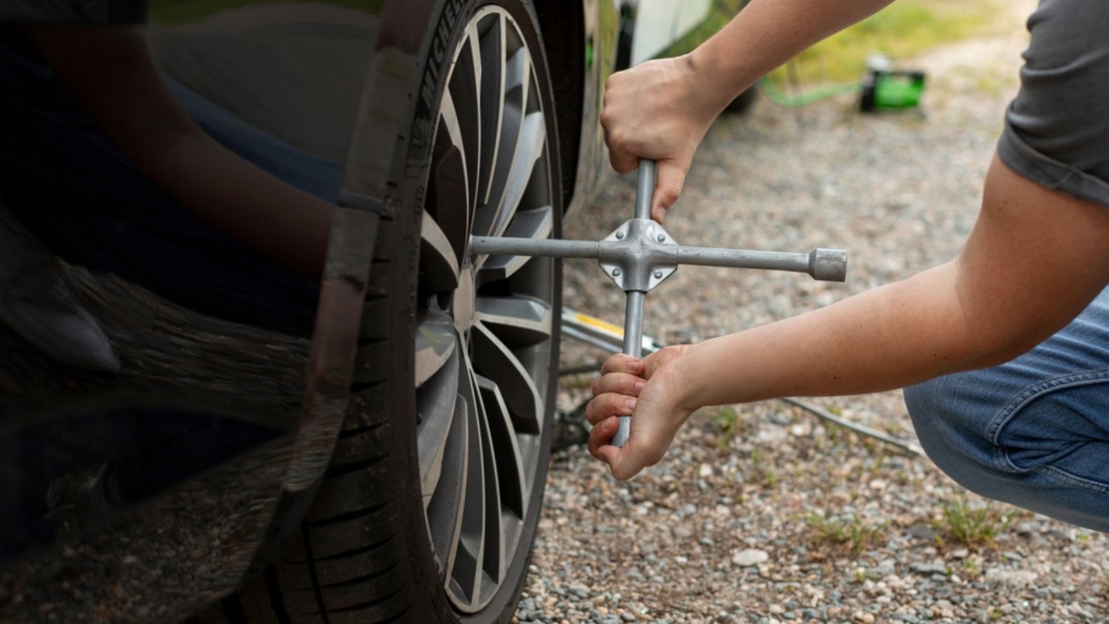 Male driver's hands with the key tightening the bolts on the wheel of his new car on road side