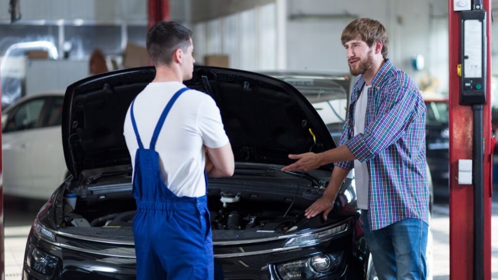 caucasian client gesturing at car to mechanic