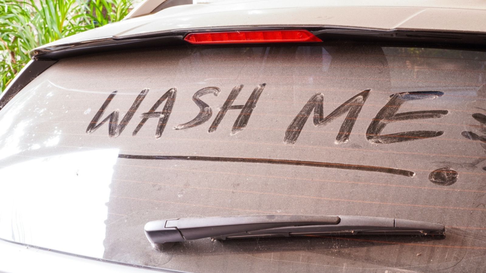 dirty car rear widescreen covered with dust with wording WASH ME