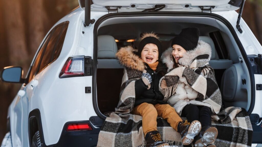 happy kids sitting in trunk covered in blanket