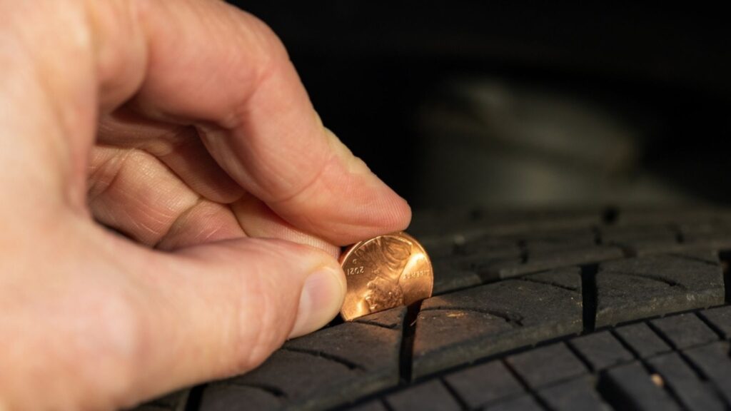 man inserting coin in tire treads. coin test