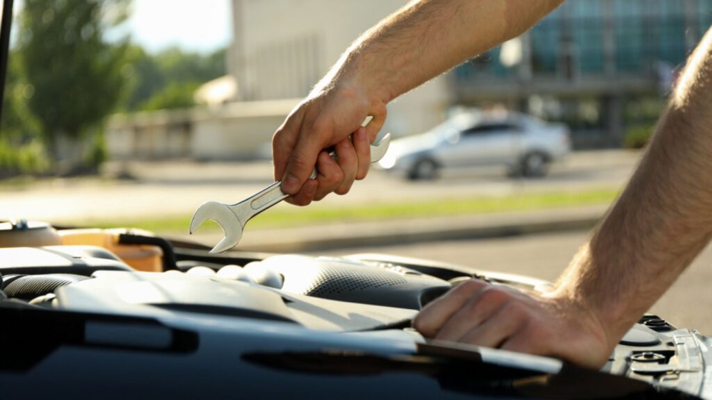 A man holds a wrench over a car engine