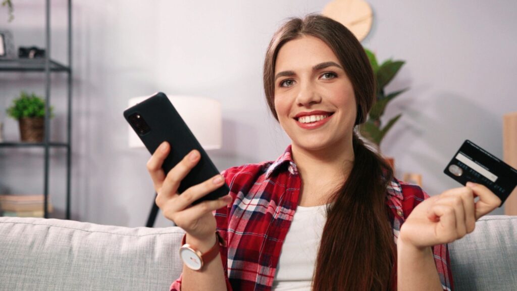 Beautiful caucasian woman sitting on sofa in living room and using smartphone while making shopping online payment
