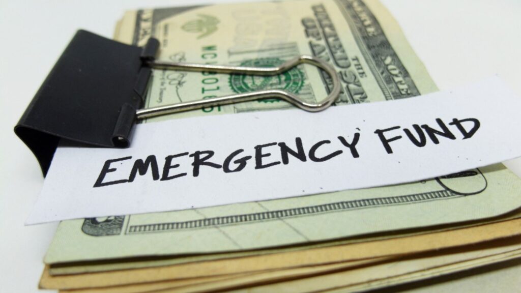 Closeup of US dollars in paper clip on white background with note written EMERGENCY FUND