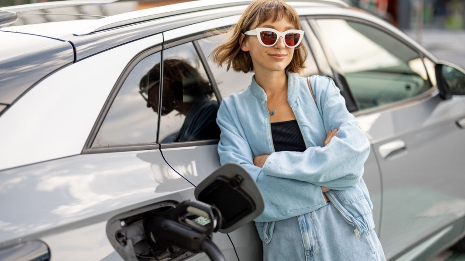 Portrait of a young woman standing near her electric car charging on a public station