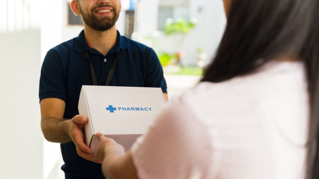 Smiling delivery man holding a white box with the word pharmacy on it while delivering medication to a woman