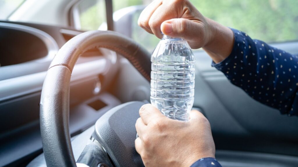 Asian woman driver holding bottle for drink water while driving a car