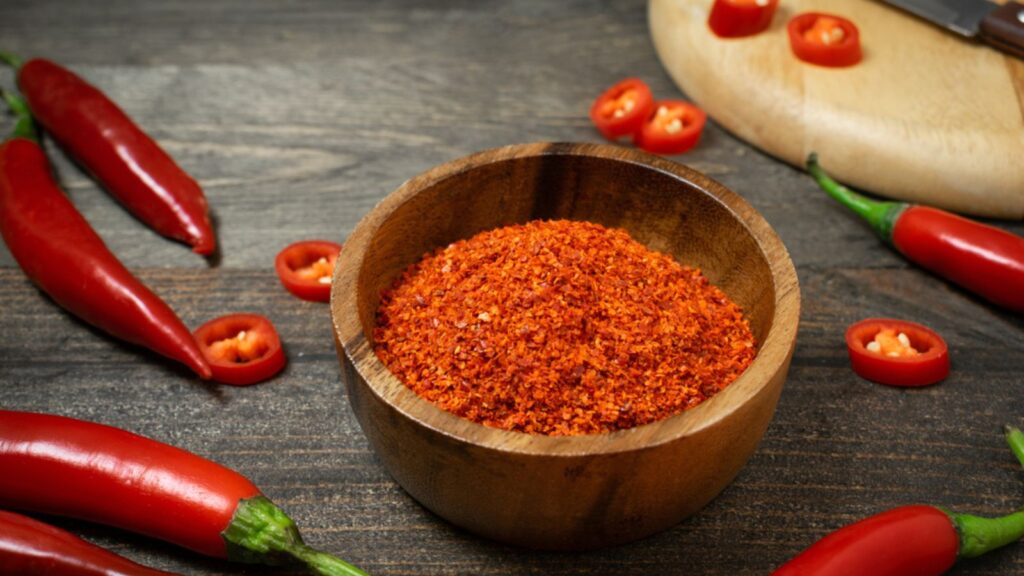 Cayenne in small bowl with chili on wooden table