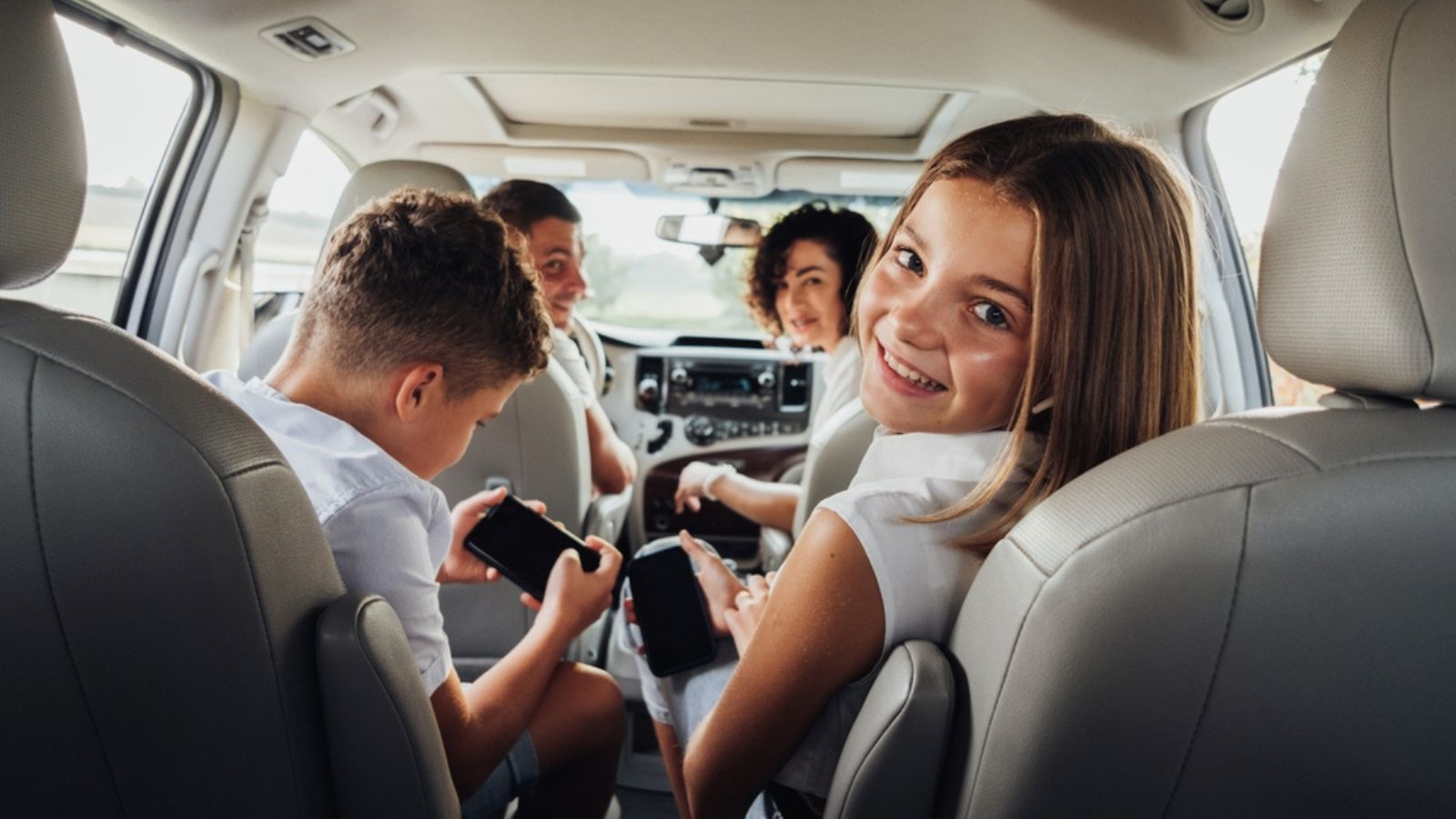 Cheerful Caucasian Teenage Girl Smiles Into Camera While Sitting in Minivan Car with Her Brother, Mother and Father