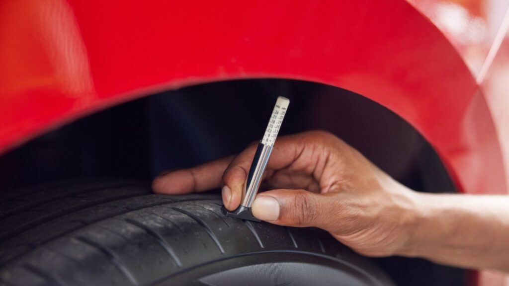 Close-Up Of Man Checking Tread On Car Tyre With Gauge