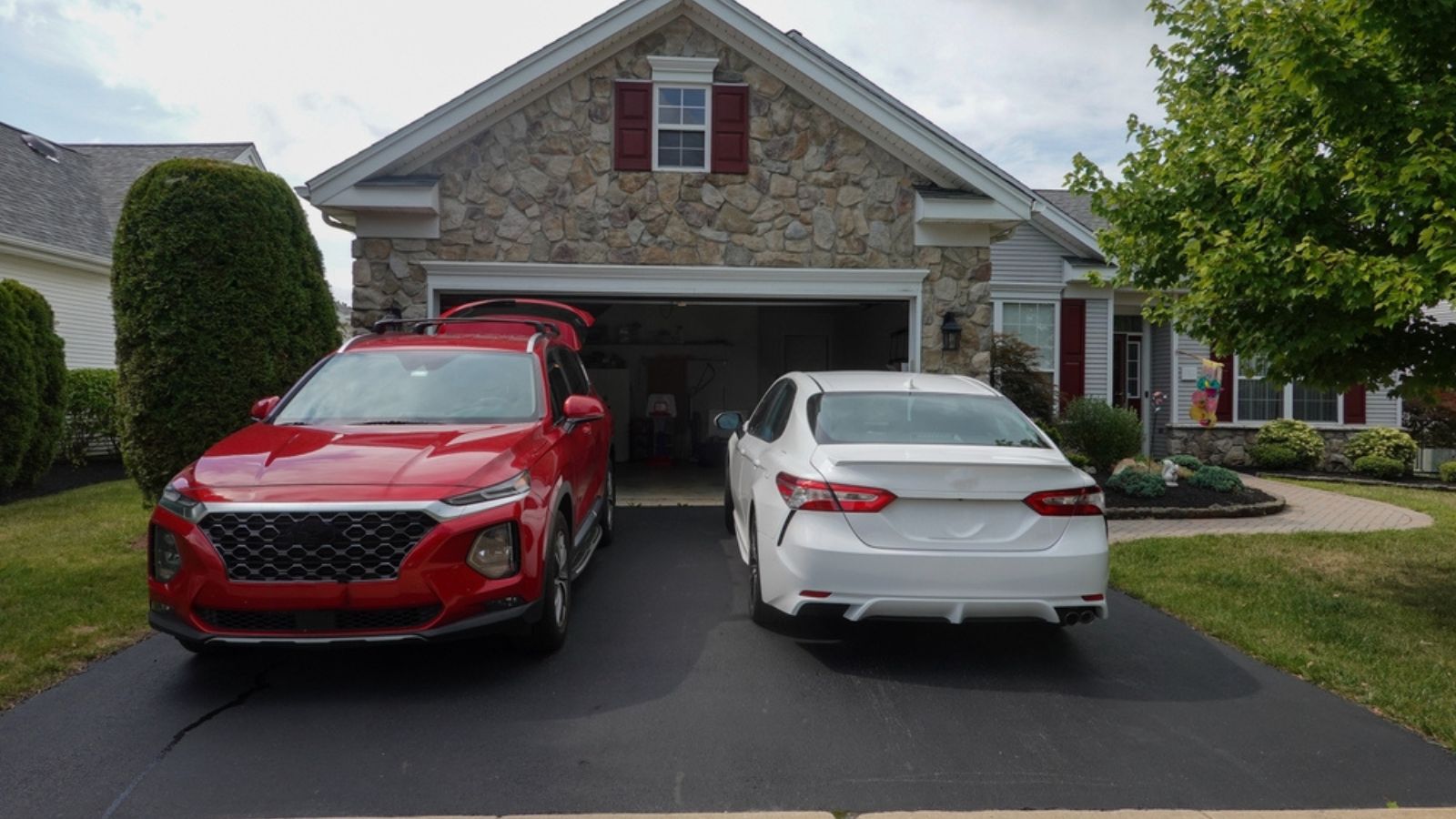 Driveway view of the stone facade of a house with two cars facing in different directions