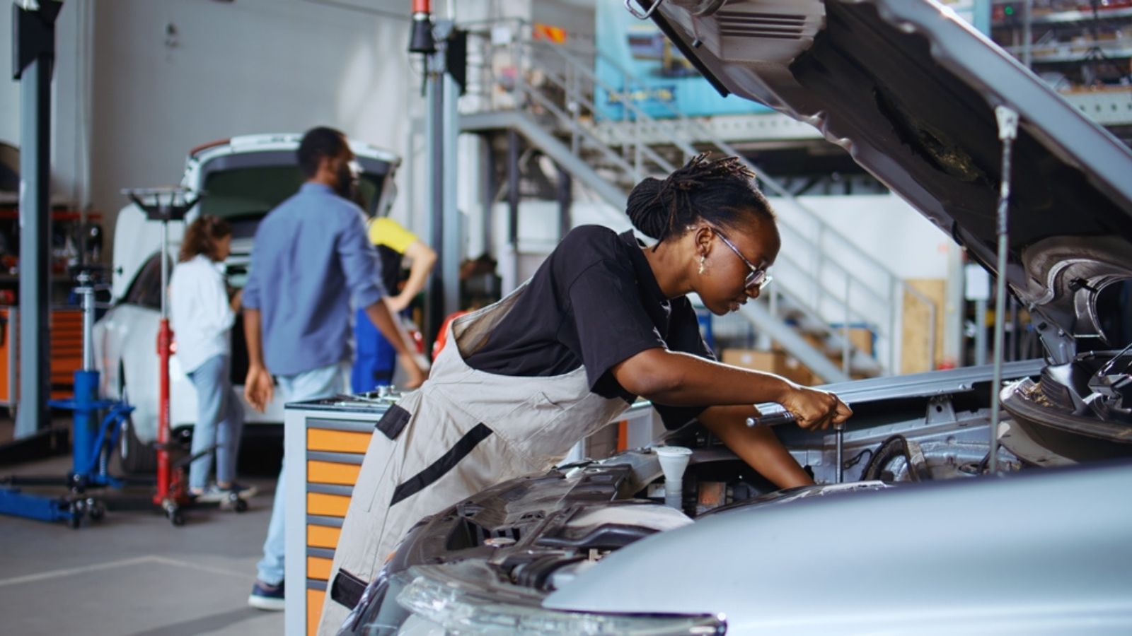 Repair shop workers using torque wrench and screwdriver to fix car in need of repairments