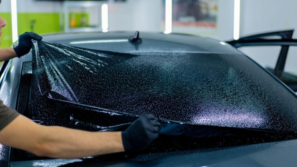 close-up of a car mechanic carefully sticking a protective tinted film on car glass detailing