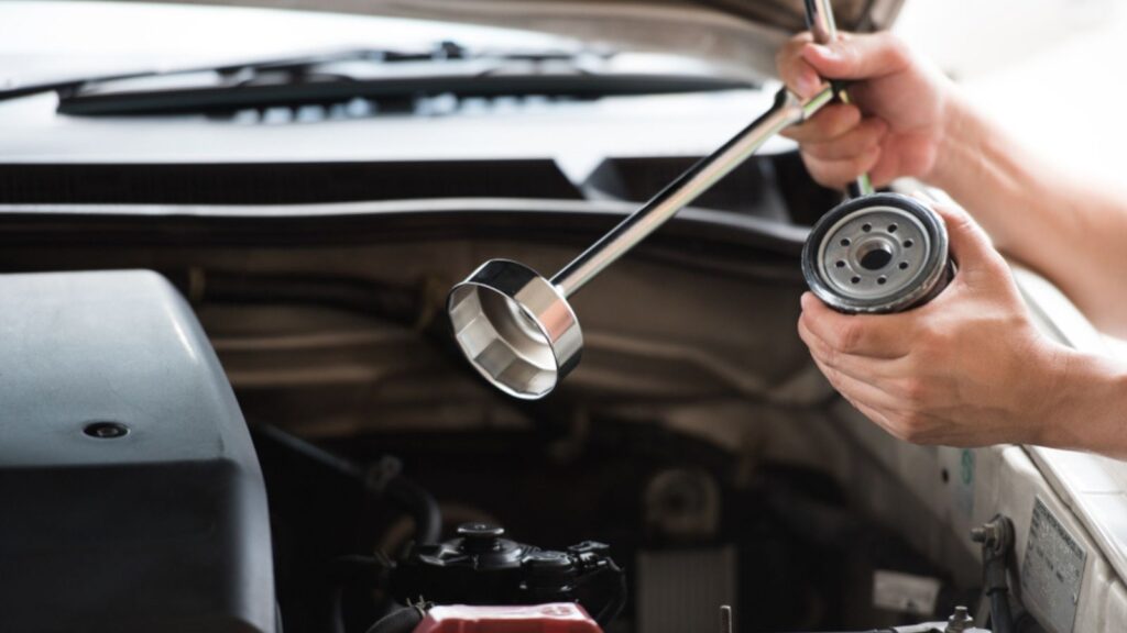 man hands holding oil filter cap wrench and automotive oil filter preparing to change the new one