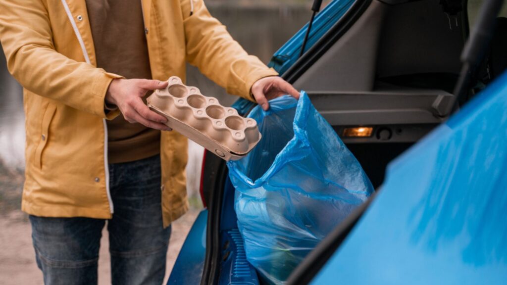 man holding carton container near blue trash bag in car