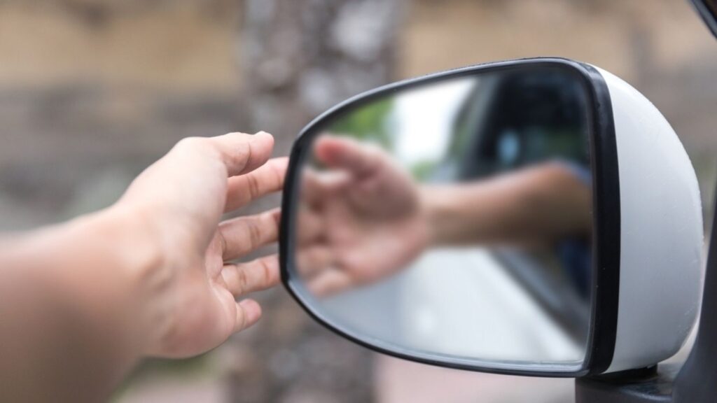 Close-up shot unrecognizable man adjusting side mirror on his car