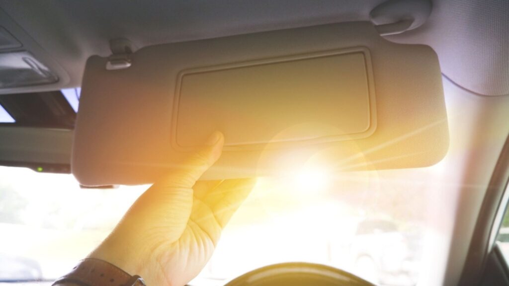Driver manually adjusting the sun visor in order to block sunlight in a car
