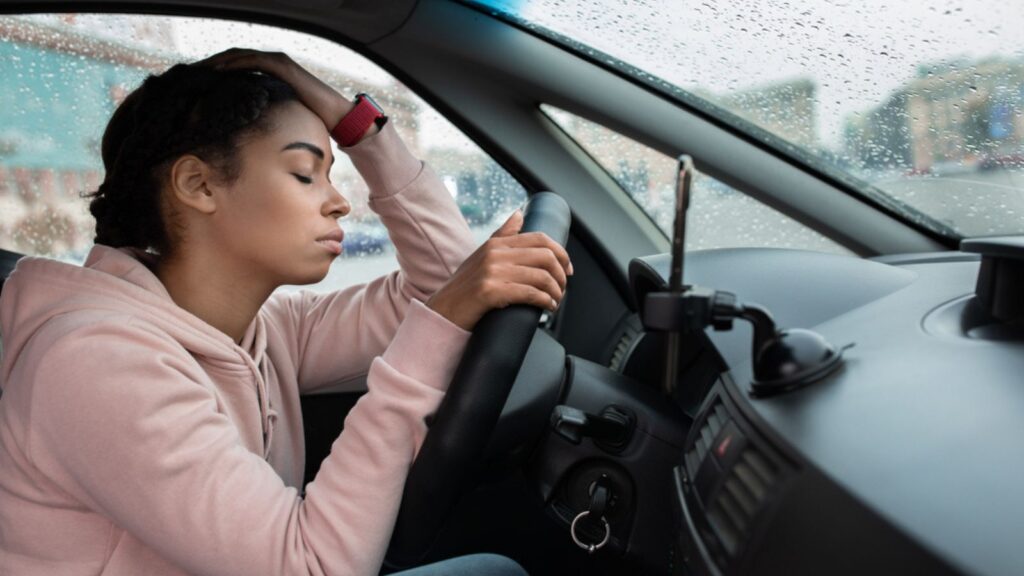 Tired sat millennial african american female with closed eyes leans on steering wheel and waits for move