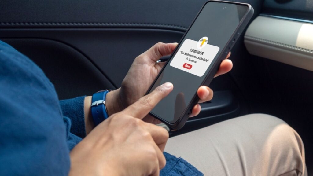 Woman in car holding a mobile phone with car maintenance schedule reminder notification on screen