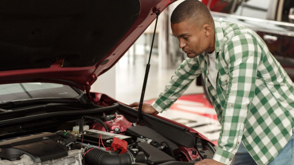 young male customer looking under the hood of a new automobile at the dealership