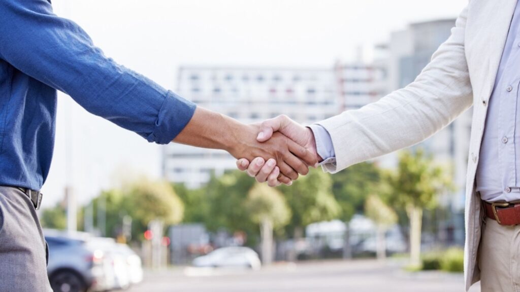 Business people, shaking hands and city introduction for travel deal, agreement or partnership in urban street