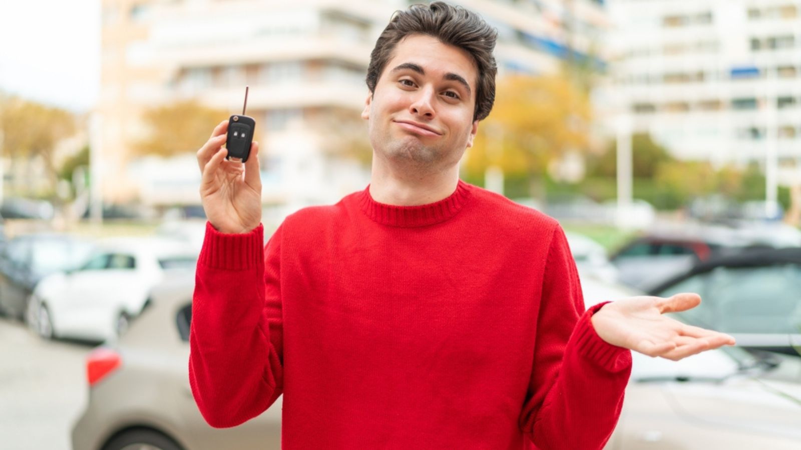 Young handsome man with car key making doubts gesture while lifting the shoulders